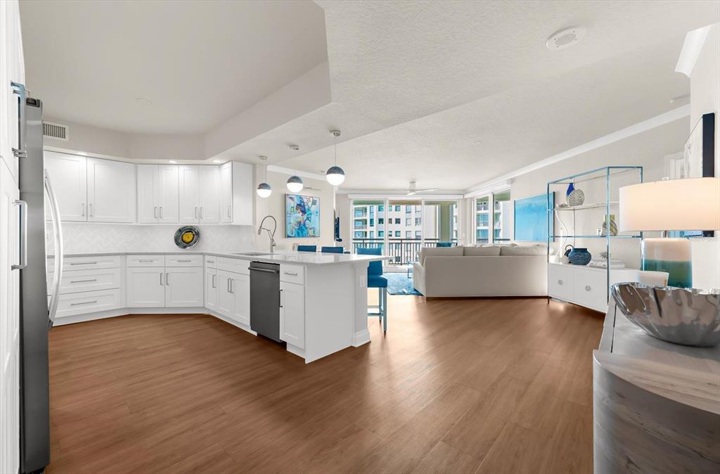 A modern open-concept kitchen and living area with white cabinets, wood floors, and balcony access — 1180 GULF BOULEVARD UNIT 1504, CLEARWATER, FL