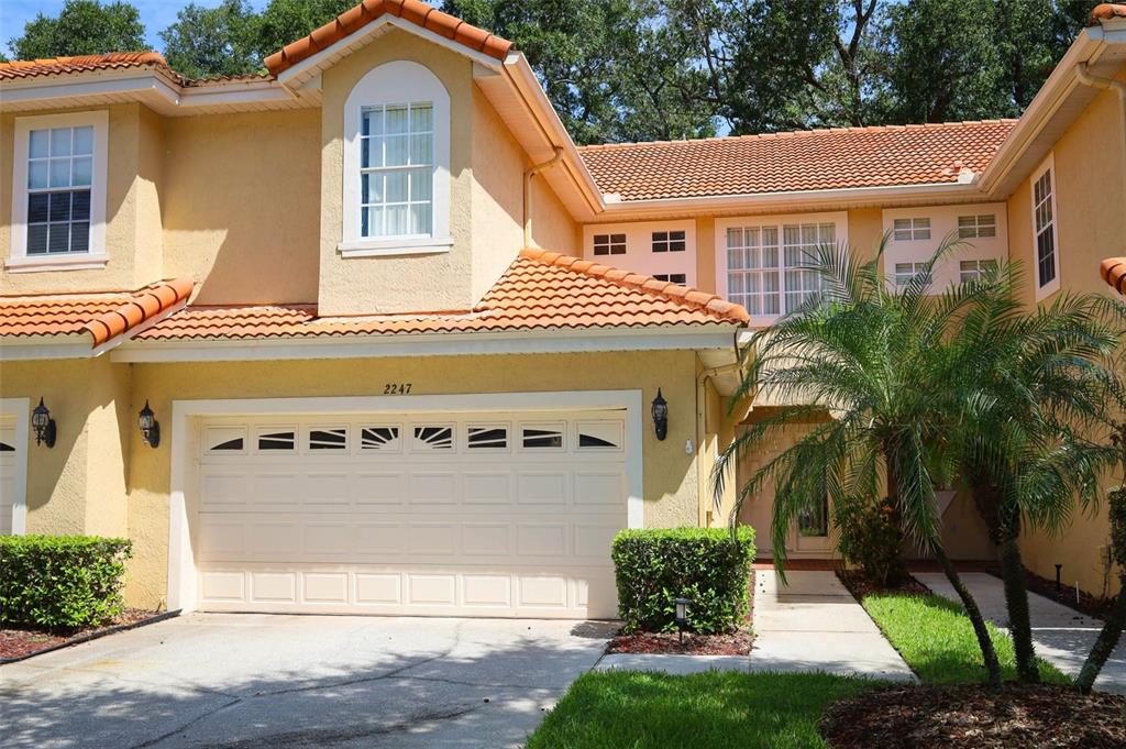 A two-story stucco townhouse with a two-car garage, tile roof, and a palm tree — 2247 WEKIVA VILLAGE LANE, APOPKA, FL