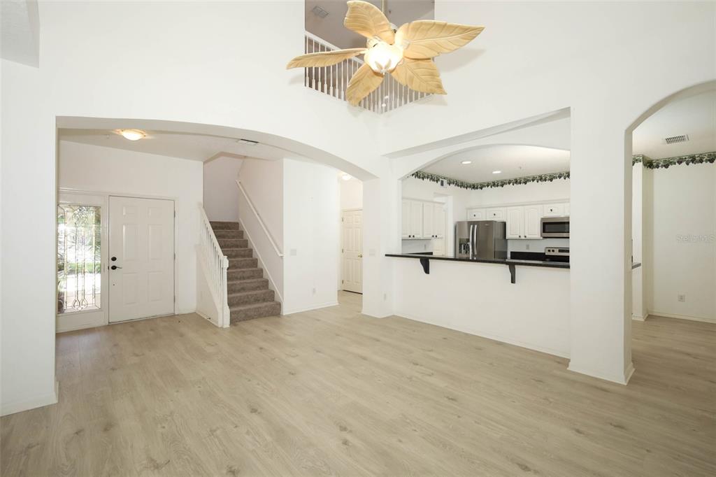 An open-concept living area with light wood flooring, a staircase, and a kitchen pass-through — 2247 WEKIVA VILLAGE LANE, APOPKA, FL