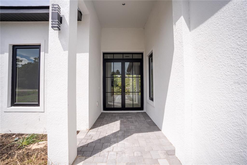 A white stucco house exterior features a paved entryway with black-framed glass double doors — 13 NEMESIA COURT E, HOMOSASSA, FL