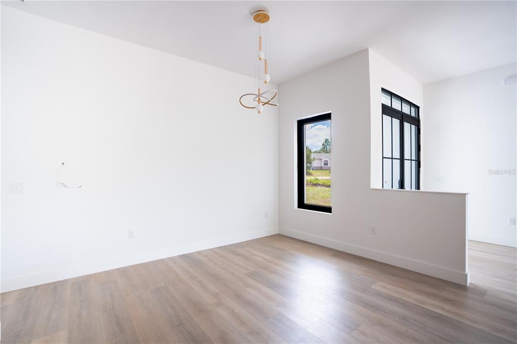 A bright, empty room features light wood-look flooring, white walls, a modern chandelier, and windows — 13 NEMESIA COURT E, HOMOSASSA, FL