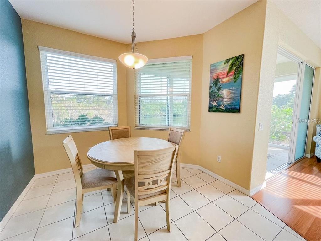 A dining nook features a round wooden table, four chairs, tile flooring, and two windows — 1802 AUBURN LAKES CIRCLE UNIT 3, VENICE, FL