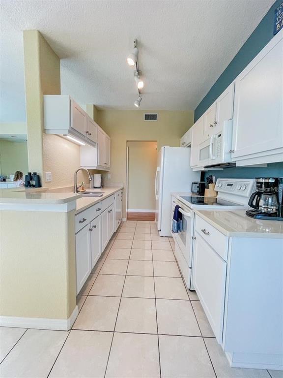 A kitchen features white cabinets, light countertops, a tile floor, and a white refrigerator — 1802 AUBURN LAKES CIRCLE UNIT 3, VENICE, FL