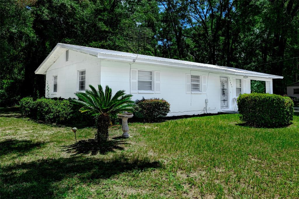 A white, single-story house with a metal roof sits on a grassy lot with trees — 17697 NW 222ND STREET, HIGH SPRINGS, FL