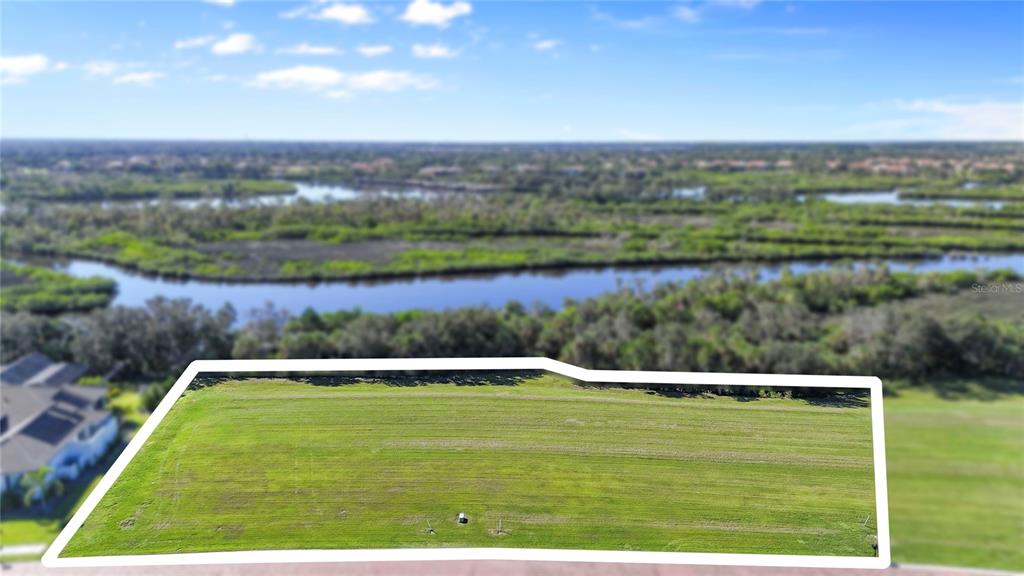 An aerial view shows a rectangular, grassy vacant lot bordered by trees and a waterway — 1628 RIO VISTA TERRACE, PARRISH, FL