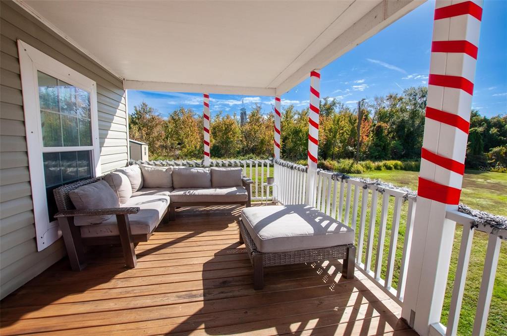 A covered wooden deck features a sectional sofa, an ottoman, and candy cane-striped support columns — 2837 NE PERSIMMON DRIVE, ARCADIA, FL