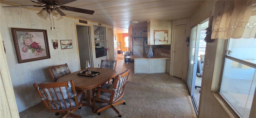 A dining area with wood-paneled walls and carpeted floors leads into a kitchen with counters — 16806 HARLEY STREET, HUDSON, FL