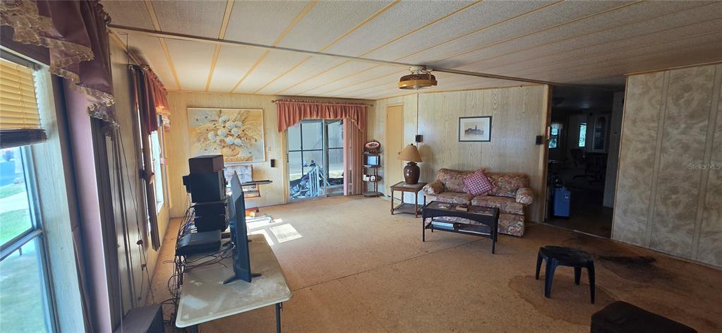 A living room with wood-paneled walls, a floral sofa, and a sliding glass door — 16806 HARLEY STREET, HUDSON, FL
