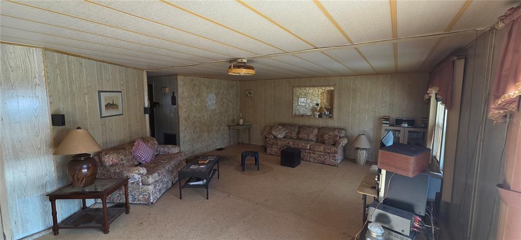 A living room features wood-paneled walls, a drop ceiling, and two floral patterned sofas — 16806 HARLEY STREET, HUDSON, FL