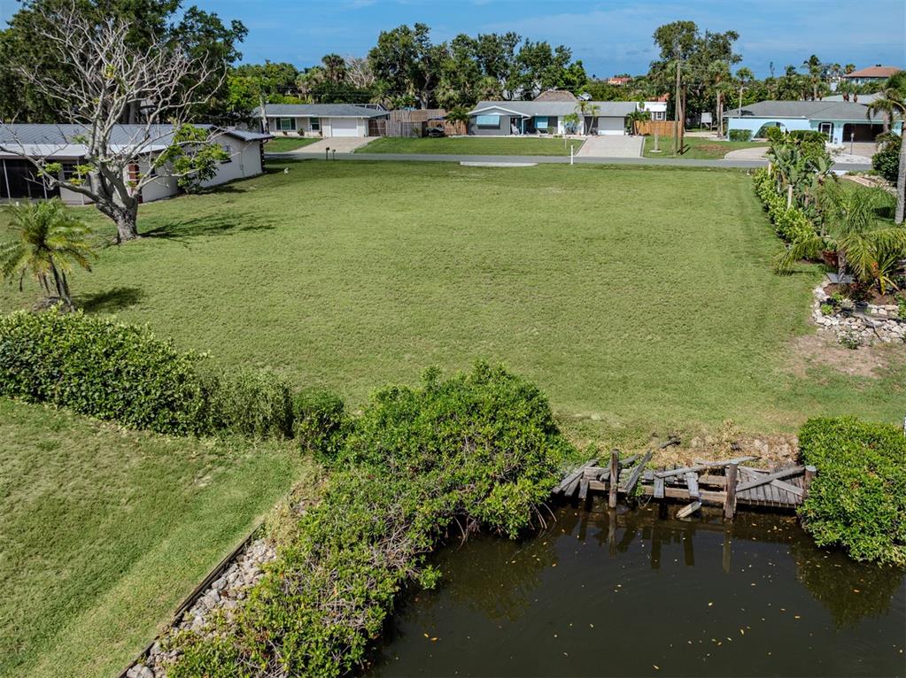 An aerial view shows a vacant grassy lot bordering a canal with a small wooden dock — 458 N SHORE DRIVE, OSPREY, FL