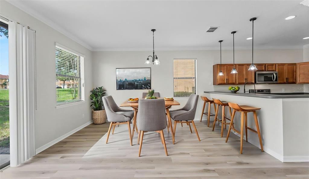 A dining area with a wooden table and grey chairs sits beside a kitchen island — 1126 CHERVIL DR, POINCIANA, FL
