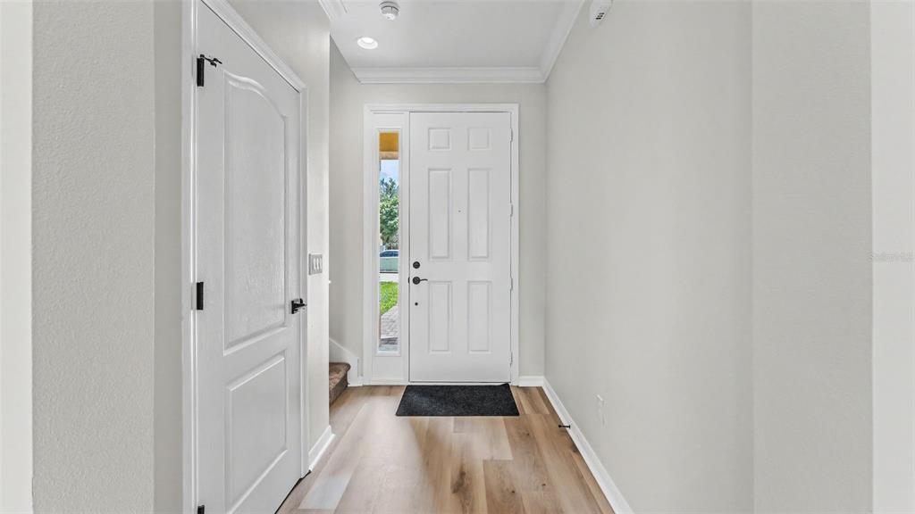 An entryway features light wood-look flooring, a white front door with a sidelight, and white walls — 1126 CHERVIL DR, POINCIANA, FL