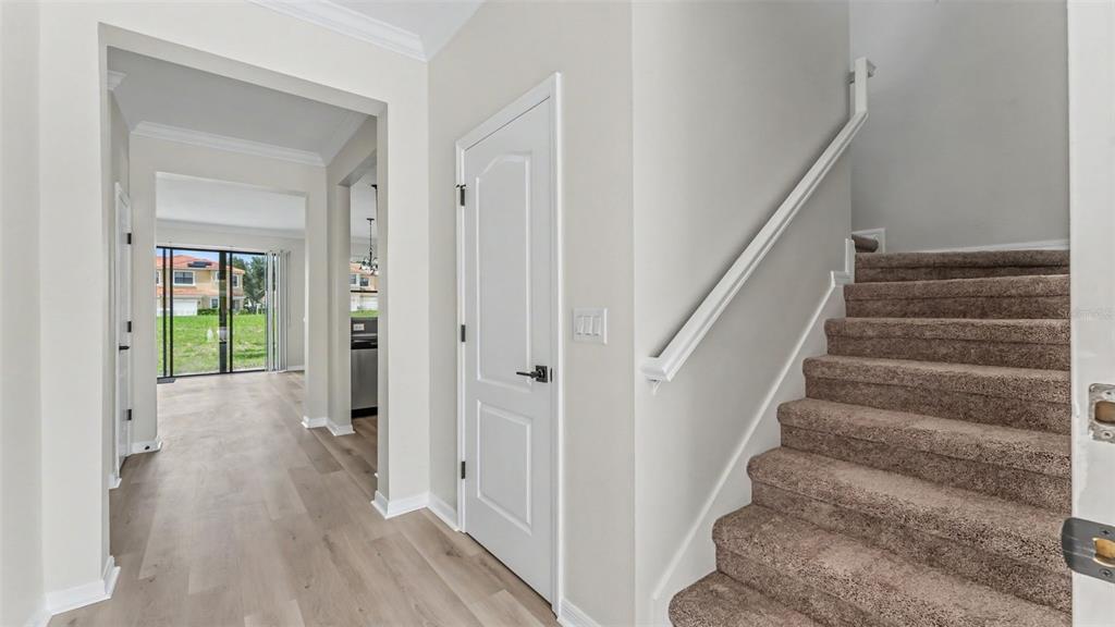 An interior entryway features light wood flooring, a white door, and carpeted stairs leading upward — 1126 CHERVIL DR, POINCIANA, FL