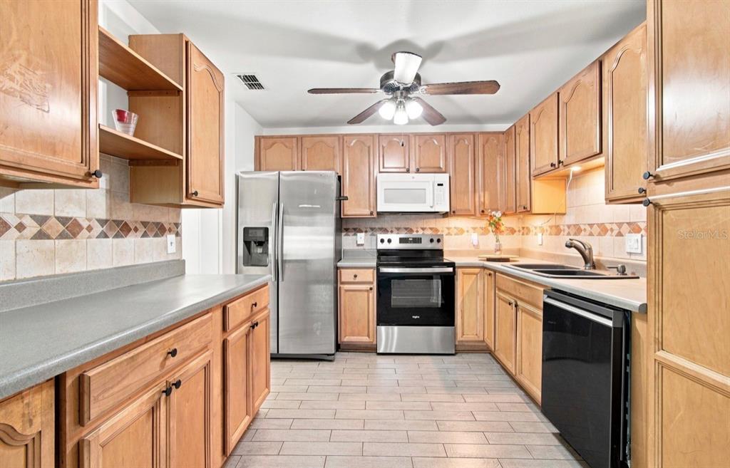 A kitchen features wood cabinets, stainless steel appliances, a tiled backsplash, and light-colored floor tiles — 1932 GREGORY DRIVE, TAMPA, FL