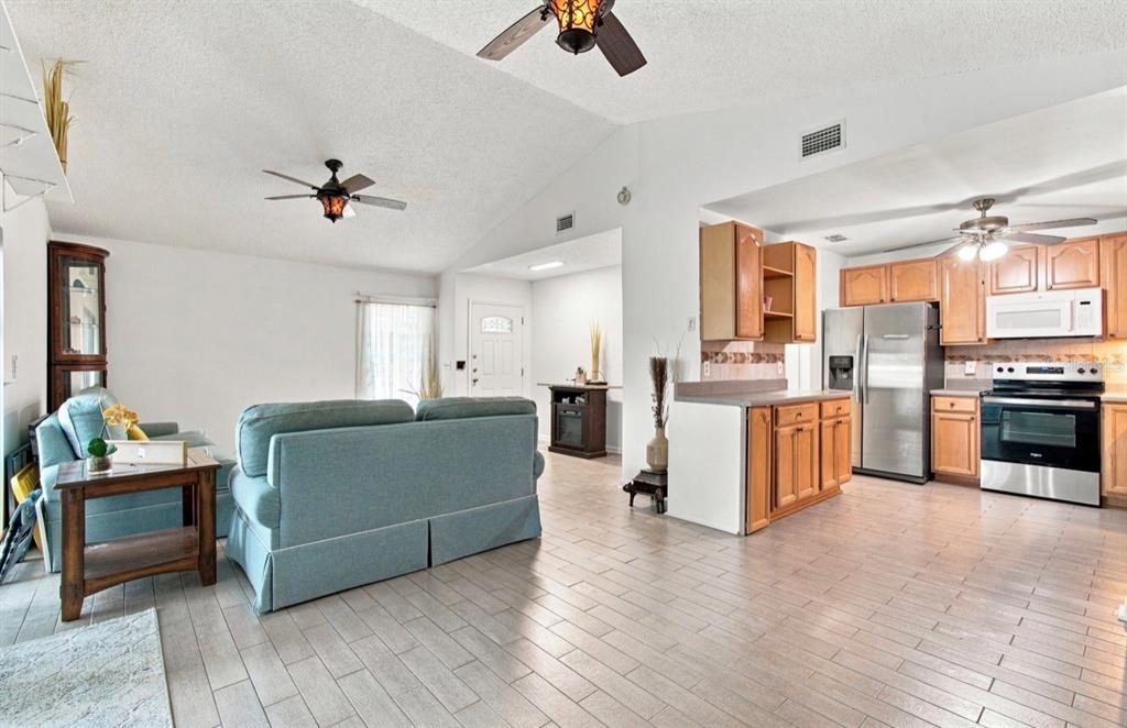 An open-concept living room and kitchen with light wood-look tile flooring and vaulted ceilings — 1932 GREGORY DRIVE, TAMPA, FL