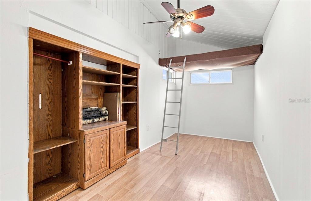 A room with wood-look flooring, a large wooden storage unit, and a loft bed with ladder — 1932 GREGORY DRIVE, TAMPA, FL