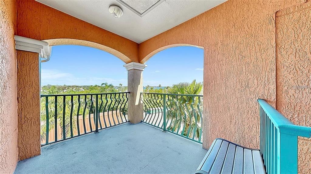 A covered balcony with textured orange walls, green metal railings, and a view of trees — 2773 VIA CIPRIANI UNIT 1330B, CLEARWATER, FL