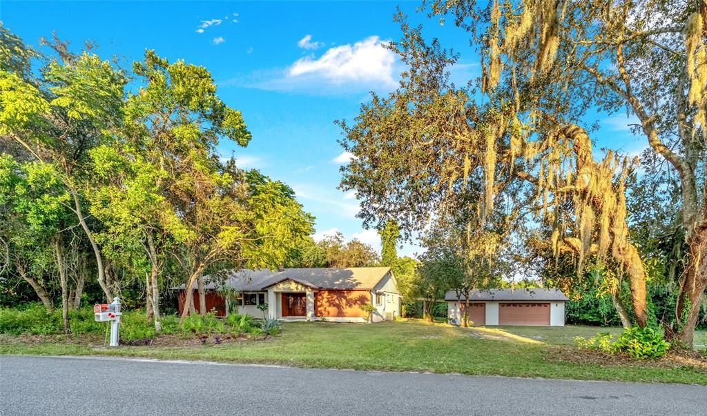 A single-story house with a detached garage sits on a grassy lot surrounded by trees — 245 AGUA VISTA STREET, DEBARY, FL