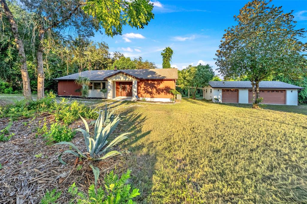 A single-story house with brown siding and a detached garage sits on a grassy lot — 245 AGUA VISTA STREET, DEBARY, FL