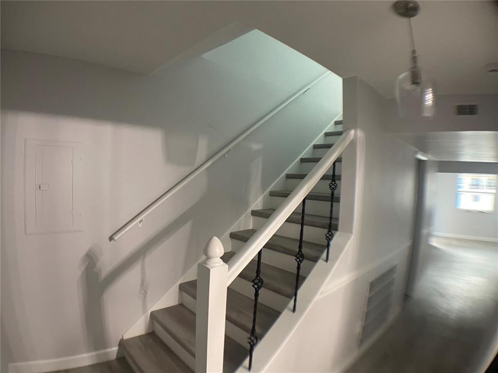 A staircase with wooden treads, white risers, and black metal balusters leads to an upper level — 152 DOUGLAS ROAD W UNIT B, OLDSMAR, FL