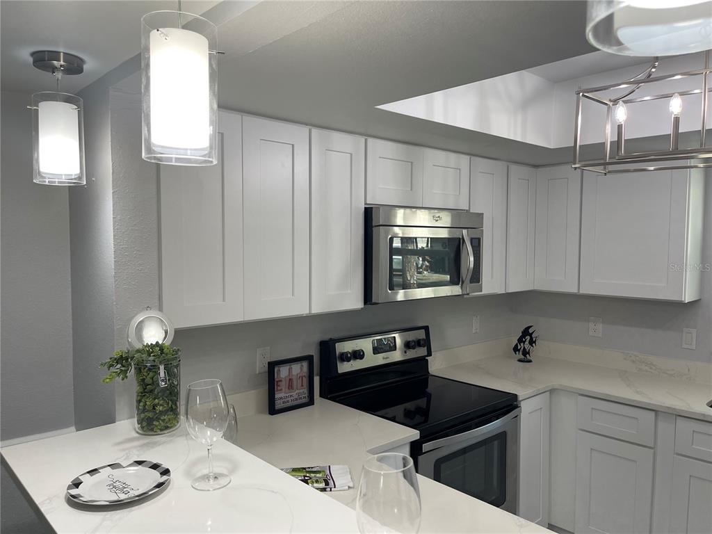 A kitchen features white shaker cabinets, stainless steel appliances, and a white quartz countertop — 152 DOUGLAS ROAD W UNIT B, OLDSMAR, FL