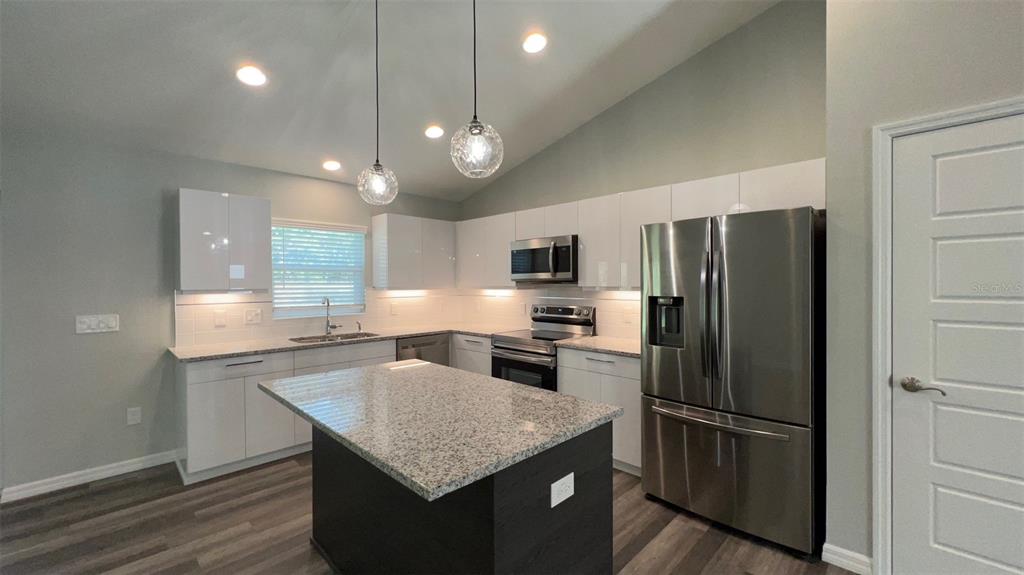 A modern kitchen features white cabinets, granite countertops, a dark island, and stainless steel appliances — TBD BAY LANE LOOP, OCKLAWAHA, FL