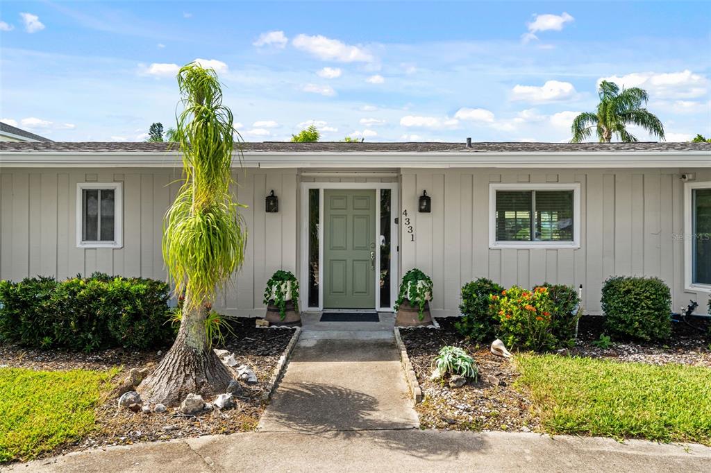 A single-story house exterior features a sage green front door, vertical siding, and landscaping — 4331 POMPANO LANE, PALMETTO, FL