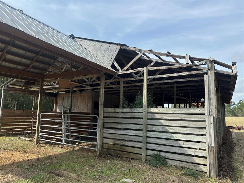 A partially damaged wooden barn structure with exposed roof rafters and horizontal slat siding — 10550 NW 115TH AVENUE, REDDICK, FL