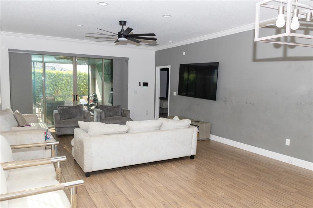 A living room features a white sofa, gray armchairs, a wall-mounted television, and wood-look flooring — 6691 ALDER ROAD, HARMONY, FL