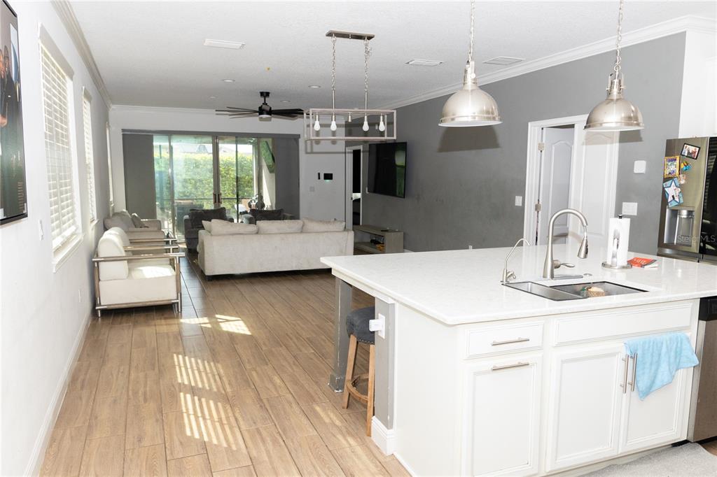 An open-concept kitchen with a white island overlooks a living area with tile flooring — 6691 ALDER ROAD, HARMONY, FL