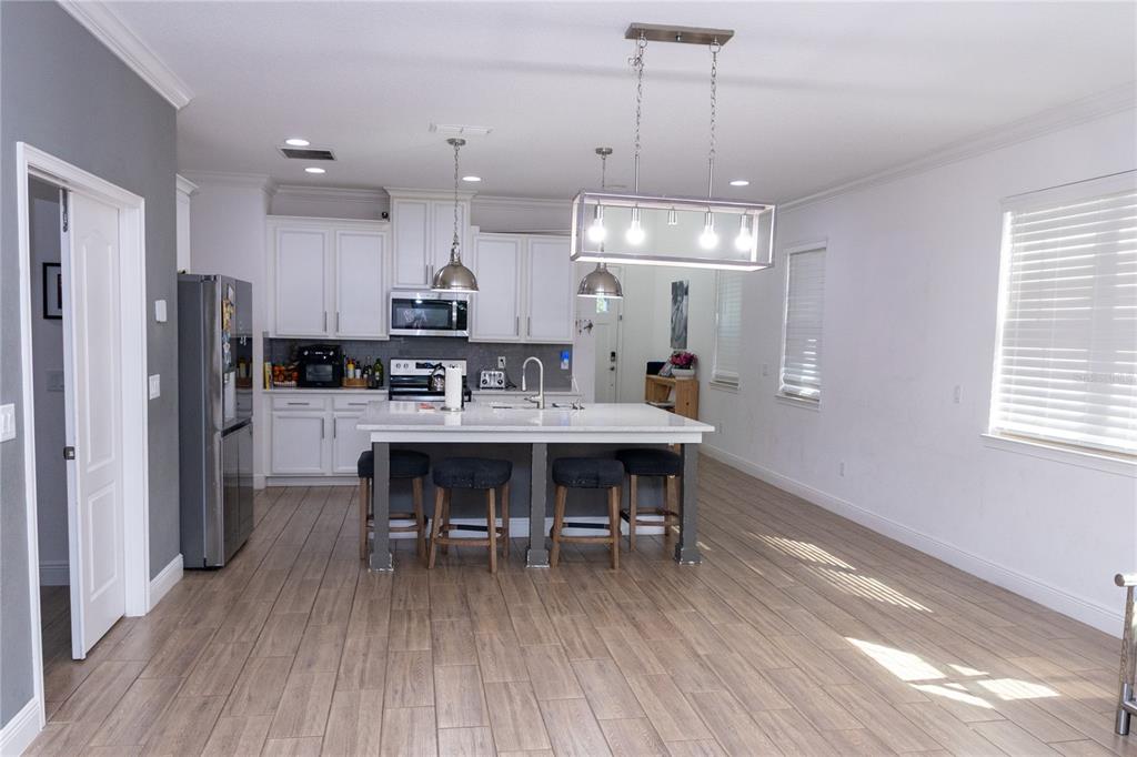 A kitchen with white cabinets, a central island with bar seating, and wood-look tile flooring — 6691 ALDER ROAD, HARMONY, FL