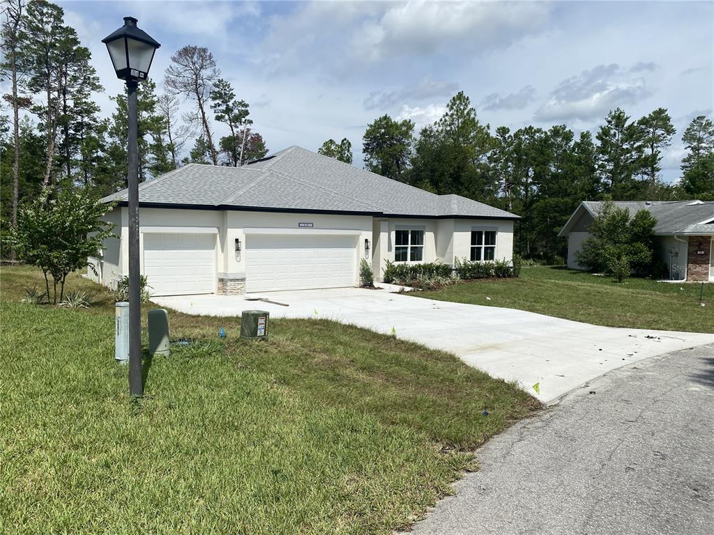 A single-story house with a white exterior, a three-car garage, and a concrete driveway — 13051 HORNBILL ROAD, BROOKSVILLE, FL