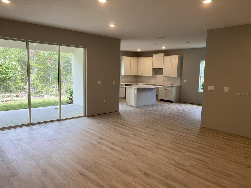 An open-concept living area features light wood-look flooring, a kitchen with white cabinetry, and sliding glass doors — 13051 HORNBILL ROAD, BROOKSVILLE, FL