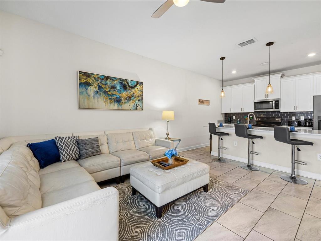 A living room with a white sectional sofa and ottoman opens to a modern kitchen — 8991 STINGER DRIVE, DAVENPORT, FL