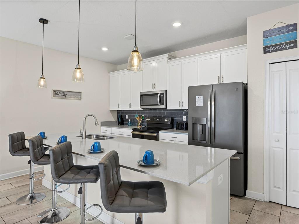 A modern kitchen features white cabinets, a quartz island with bar seating, and stainless appliances — 8991 STINGER DRIVE, DAVENPORT, FL