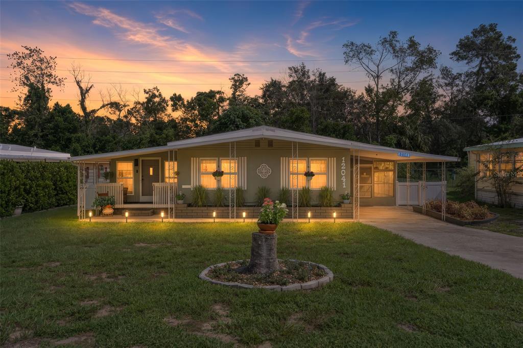 A single-story house with a green exterior, a front porch, and a landscaped yard at dusk — 12041 FAIRWAY AVENUE, BROOKSVILLE, FL