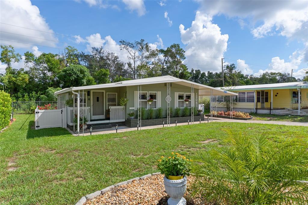 A light green manufactured home features a covered front porch and a gravel landscaping bed — 12041 FAIRWAY AVENUE, BROOKSVILLE, FL