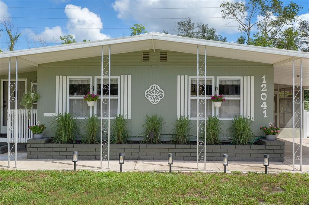 The exterior of a green mobile home features a brick planter and decorative metal supports — 12041 FAIRWAY AVENUE, BROOKSVILLE, FL