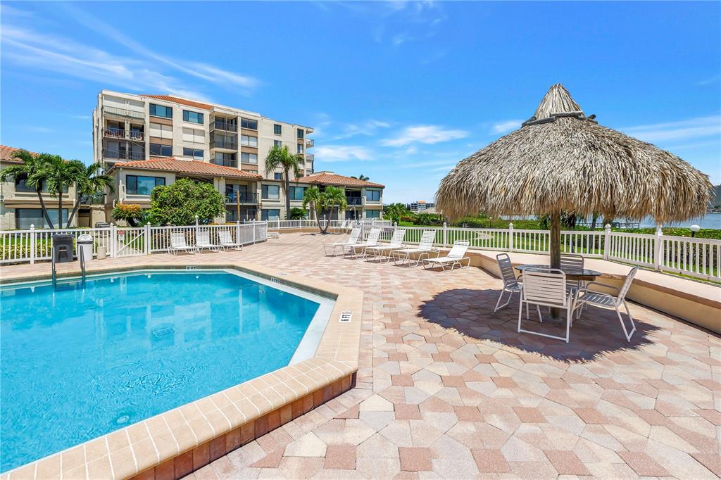 A swimming pool with a tiki hut and lounge chairs on a paved patio area — 6269 PALMA DEL MAR BOULEVARD S UNIT 508, ST PETERSBURG, FL