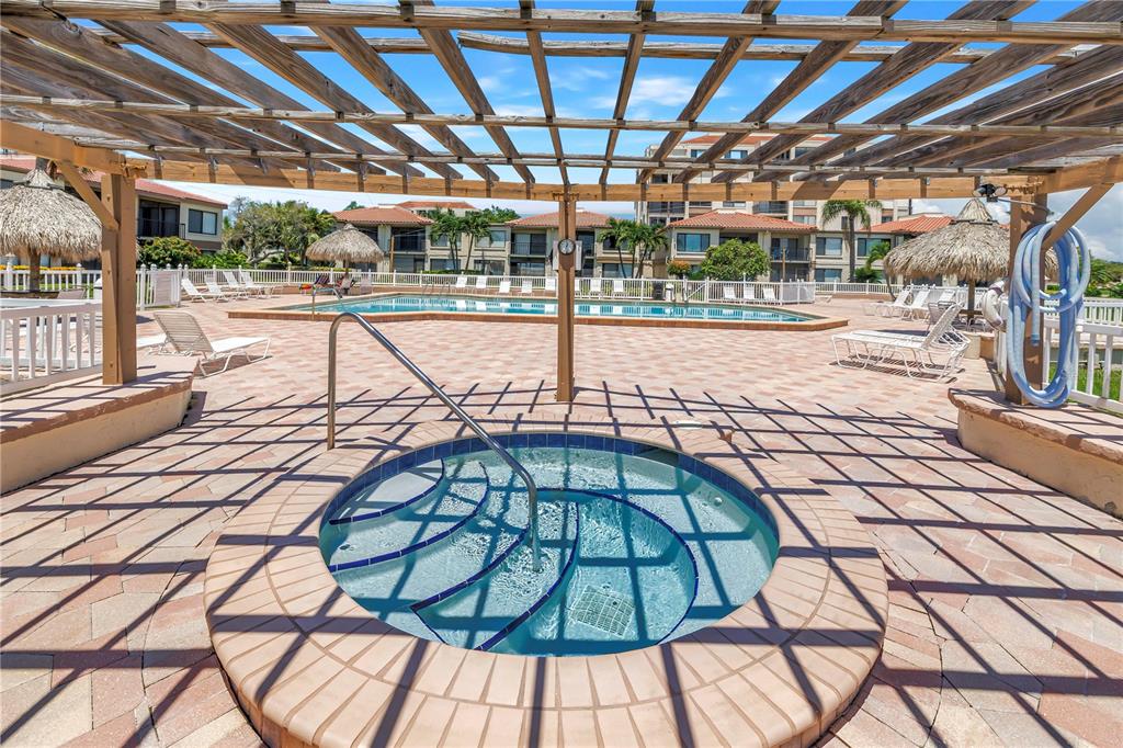 A circular hot tub sits on a paved patio beneath a wooden pergola near a pool — 6269 PALMA DEL MAR BOULEVARD S UNIT 508, ST PETERSBURG, FL