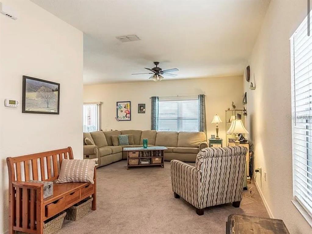 A living room features a beige sectional sofa, a patterned armchair, and a wooden bench — 12316 NE 48TH LOOP, OXFORD, FL