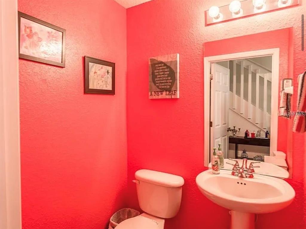 A powder room features bright red walls, a pedestal sink, and a wall-mounted light fixture — 12316 NE 48TH LOOP, OXFORD, FL