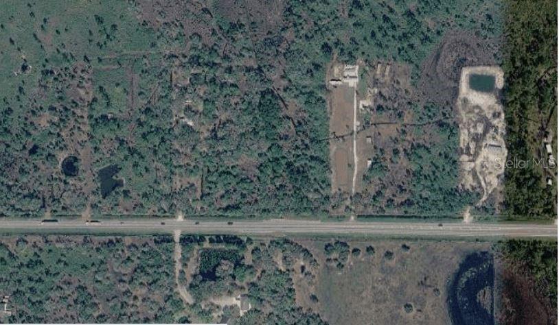 An aerial view shows a rural property with a highway, wooded areas, and cleared land — 20901 STATE ROAD 60 E, LAKE WALES, FL