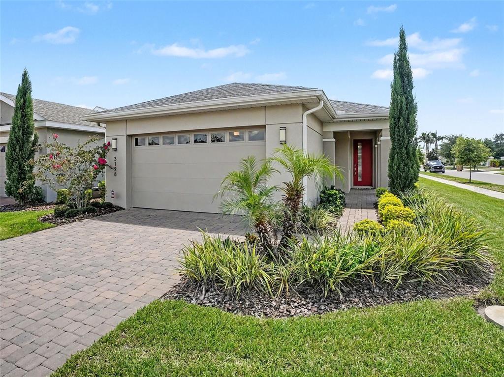 A single-story house with a beige exterior, a red front door, and a paved driveway — 3128 SONGBIRD CIR, HARMONY, FL