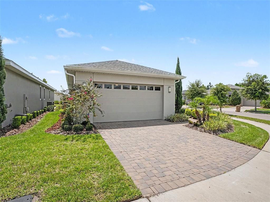 A beige house exterior features a two-car garage, a paver driveway, and landscaped front yard — 3128 SONGBIRD CIR, HARMONY, FL