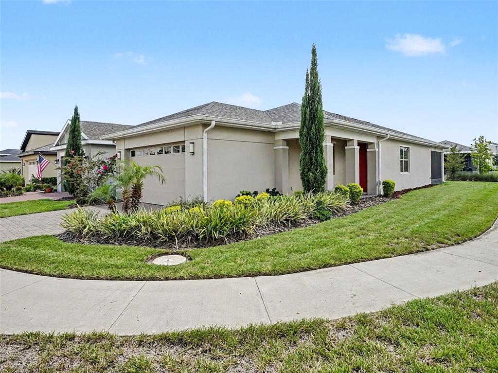 A beige single-story house with a two-car garage, a red front door, and landscaped yard — 3128 SONGBIRD CIR, HARMONY, FL