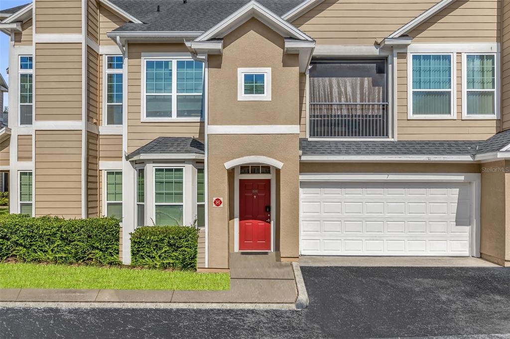 A two-story townhouse exterior features a red front door, a garage, and tan siding — 1980 ERVING CIRCLE UNIT 111, OCOEE, FL