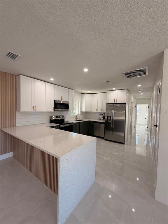 A modern kitchen with white cabinets, stainless steel appliances, and a slatted wood kitchen island — 2405 21ST AVE W, BRADENTON, FL
