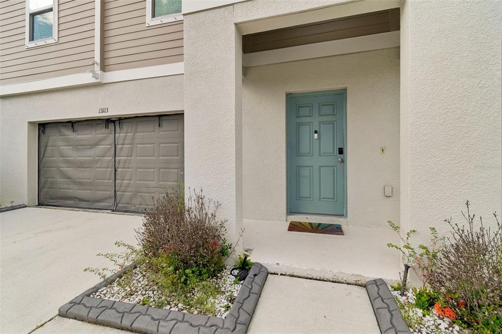 A light-colored townhouse exterior features a blue front door, a garage, and a small garden — 13113 FRUITVILLE WAY, RIVERVIEW, FL