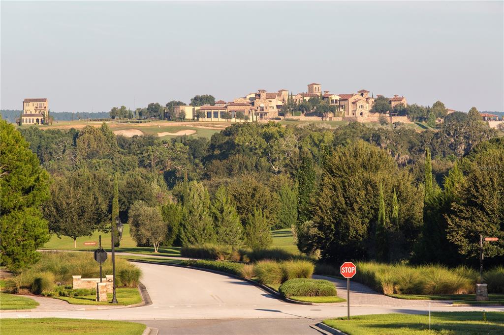 A paved road leads toward a large stone estate situated on a distant grassy hill — 16123 PENDIO DRIVE, BELLA COLLINA, FL